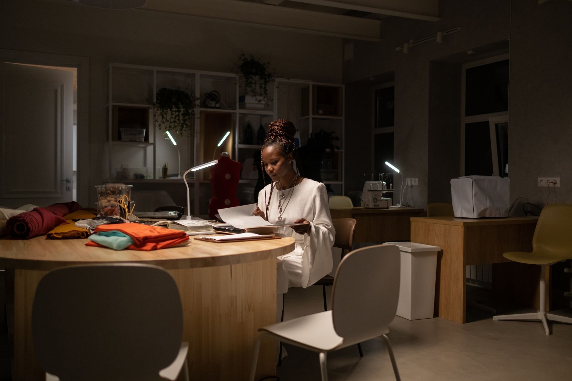 A focused fashion designer working late in a stylish, well-lit studio with sewing materials.